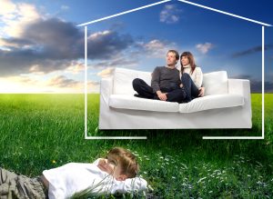 Young couple sitting on a sofa surrounded by the form of a house and smiling child lying on green meadow