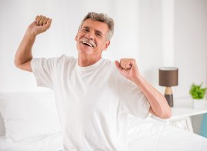Portrait of smiling mature man is stretching his arms on bed.