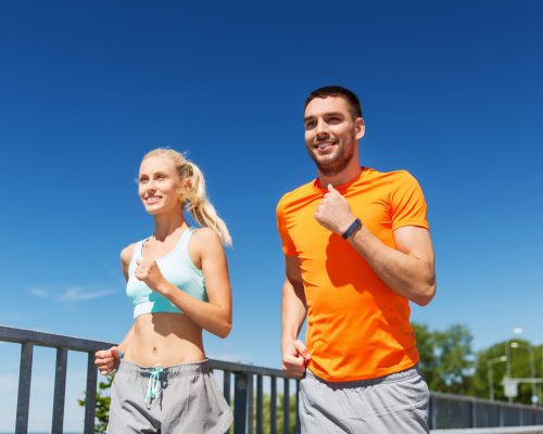 fitness, sport, friendship and healthy lifestyle concept - smiling couple with heart-rate watch running at summer seaside